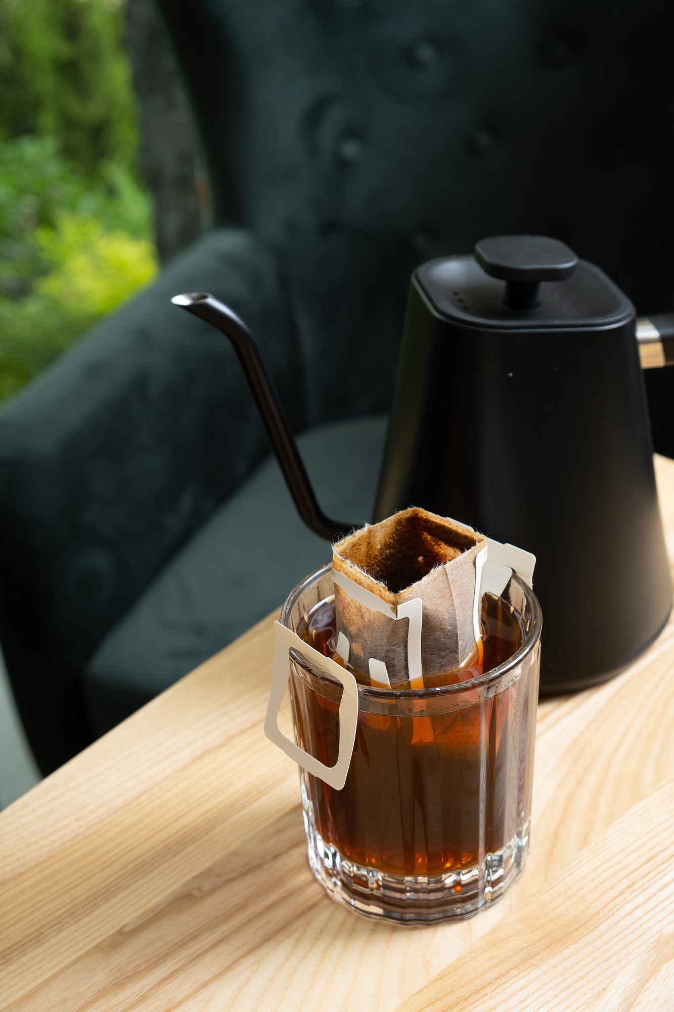 Glass cup with making coffee from drip bag on wooden table. Trends in making coffee at home.